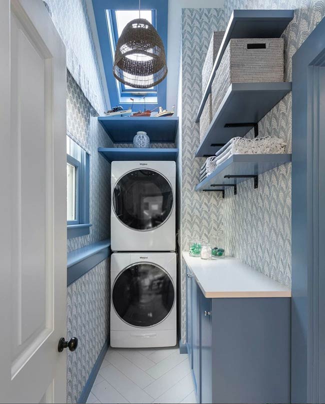 Bright blue cabinets and white open shelving bring energy to this narrow laundry room. Stacked Whirlpool appliances fit perfectly, and wallpapered walls add texture. A skylight above brightens the space, while clever storage ensures everything stays organized. Even compact laundry rooms can feel cheerful and efficient with thoughtful color choices.