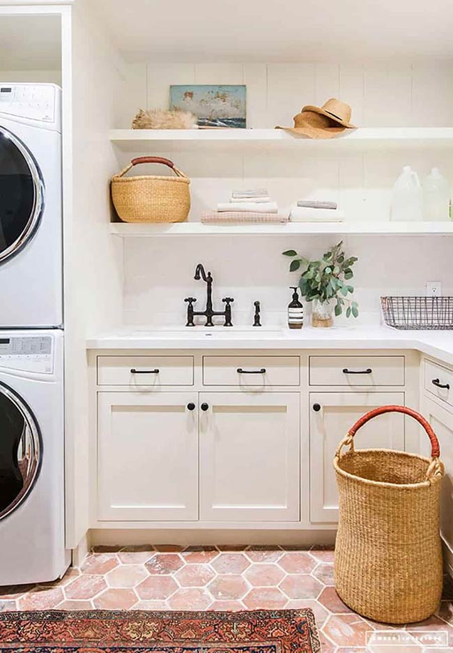 Terra cotta floors and wooden baskets add warmth and texture. Tall cabinets and open shelves keep laundry supplies organized, while a stackable washer/dryer ensures efficiency. The combination of materials and textures makes the space feel cozy without sacrificing practicality.