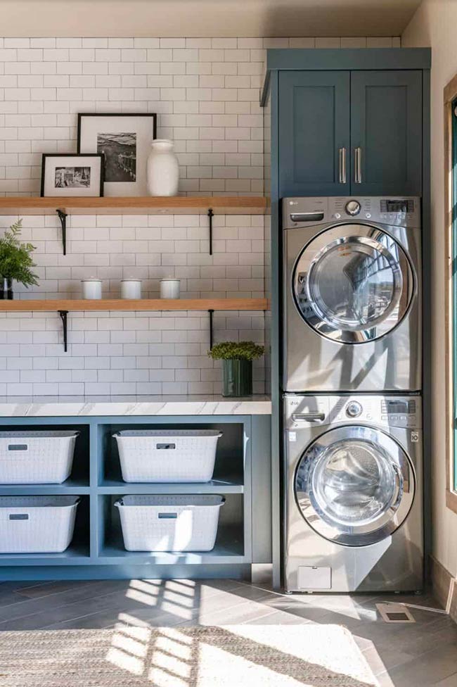 Natural light floods this well-planned laundry space, making it feel open and airy. Soft blue cabinets and floating shelves add charm, while stackable appliances save floor space. Sunlight makes folding clothes or sorting laundry more pleasant, proving that a simple window can make a huge difference.