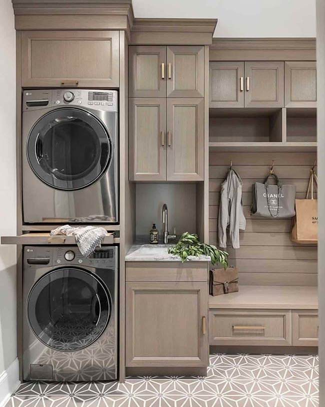 In this Chicago laundry room, a pull-out folding shelf sits neatly between the stacked washer and dryer. It’s perfect for folding clothes immediately after drying, saving time and preventing wrinkles. White oak cabinets with subtle grain add warmth, while clean hardware keeps the space modern. A white under-mount sink nearby makes pre-treating stains simple. Even in a medium-size room, clever features like a folding shelf make chores feel effortless and efficient. Functional details like these help turn everyday laundry into a smoother, more organized task.