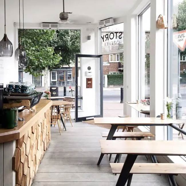The honeycomb pattern on the light wood counter adds such a cool texture to the room. Huge glass windows wrap around the corner, letting in tons of natural light to make this coffee shop interior feel open and airy.