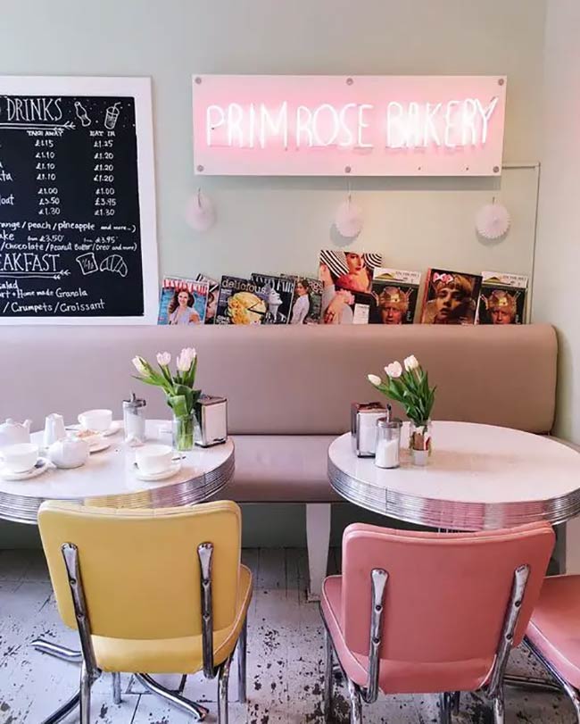 This cafe has a strong 1950s diner feel. Mint-green walls and a plush pink banquette create a playful atmosphere. The glowing pink neon sign and chrome-trimmed furniture complete the retro look.