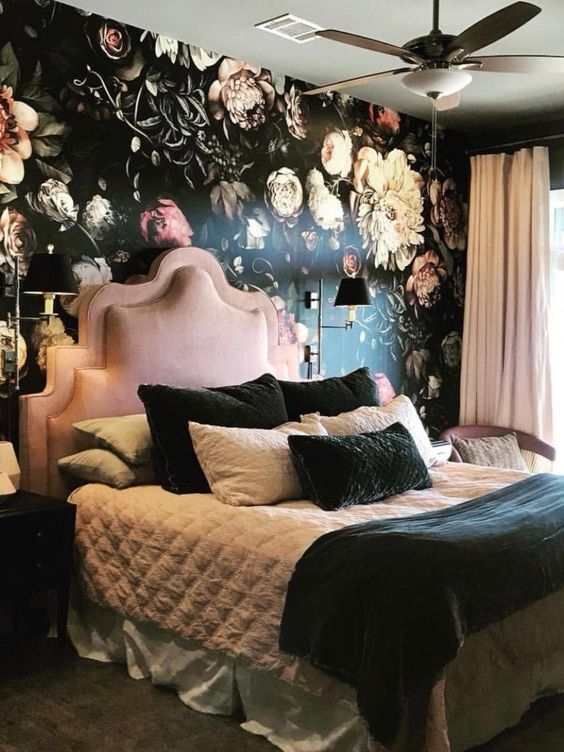 Dark floral wallpaper is a stunning choice for a feature wall. The tall pink headboard looks very comfortable nestled among the deep colors. This pink and black bedroom has a wonderful, moody atmosphere.