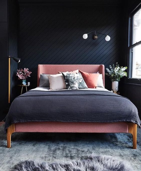 The diagonal lines on the black wall create a really cool texture behind the bed. A pink fabric bed frame pops out against the dark color. It is a simple but very stylish pink and black bedroom.