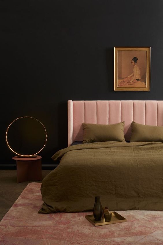 A glowing ring light creates a unique mood next to the soft pink velvet headboard. This pink and black bedroom keeps things minimal and elegant.
