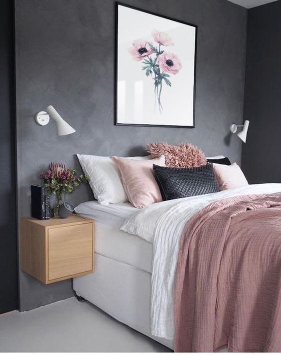 Textured grey walls give this space a soft, industrial vibe. The wooden floating nightstand is a smart way to save floor space. With the flower art and the waffle blanket, this pink and black bedroom feels very relaxing.