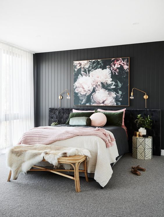 The black wood paneling on the wall adds so much texture behind the bed. That huge flower painting brings all the colors together beautifully. I love how the geometric nightstand adds a modern touch to the corner. This pink and black bedroom looks super comfortable and stylish.