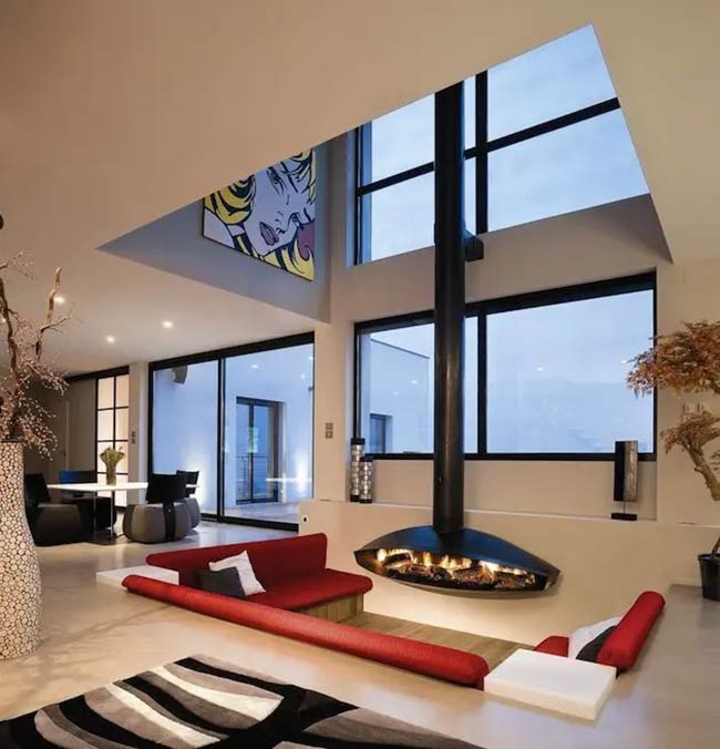 That hanging black fireplace is the center of this conversation pit. The bright red sofa looks sharp. Look at the big cartoon painting way up high!