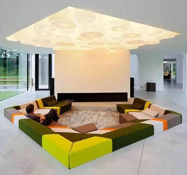 What a fun, colorful couch! This square conversation pit uses green, yellow, and orange blocks for seats. The huge light on the ceiling makes the whole space glow.