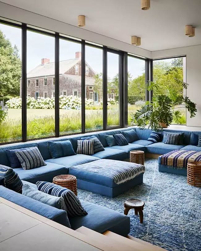 A huge blue sofa fills this entire conversation pit. The giant windows let you see the whole yard. This space looks perfect for a big group.