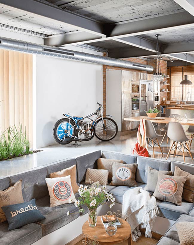 Putting a motorcycle in the living room is a wild idea! This gray conversation pit has cool pillows and fits right in with the industrial-style ceiling.
