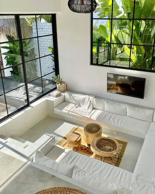This is a very bright and white conversation pit. The seating is just white cushions built right into the floor. Giant windows let in a lot of sun.