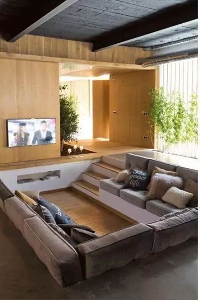 This conversation pit is very deep, with lots of stairs to get down. The gray sofas look comfortable for watching TV.