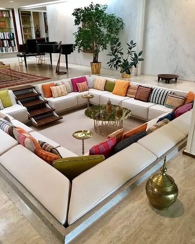 Look at all the colorful pillows on the white sofa! This is a very large square conversation pit with wooden steps.