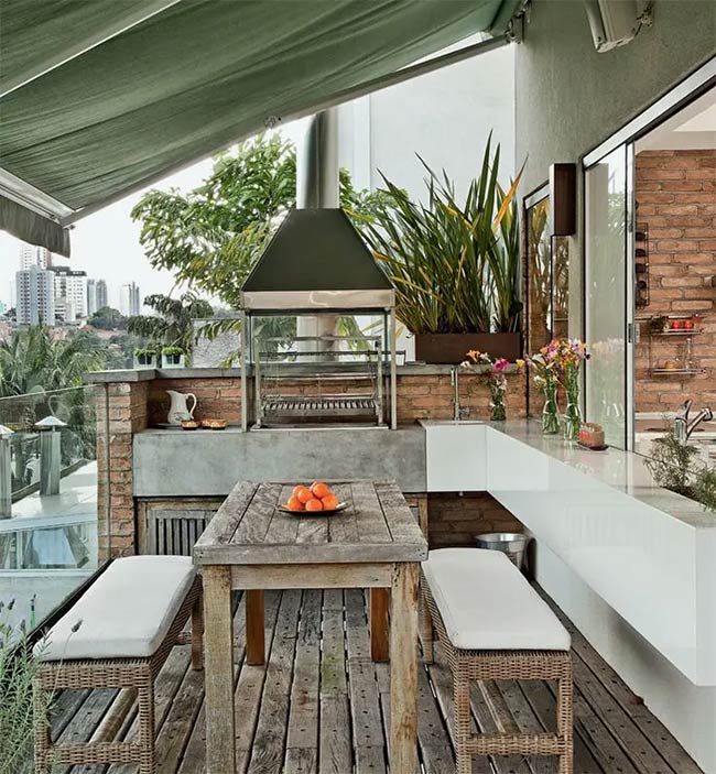 This balcony makes great use of space with a built-in brick grill and a rustic wooden table. A green awning protects the dining area from the sun while you enjoy the city view. It is a charming spot for a small lunch.