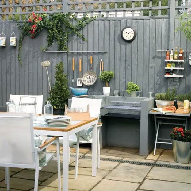 Painting the wooden fence grey creates a modern backdrop for this simple outdoor kitchen. Hanging pots and utensils on the wall keeps the small counter clear for cooking. It’s a smart and budget-friendly way to style a patio.