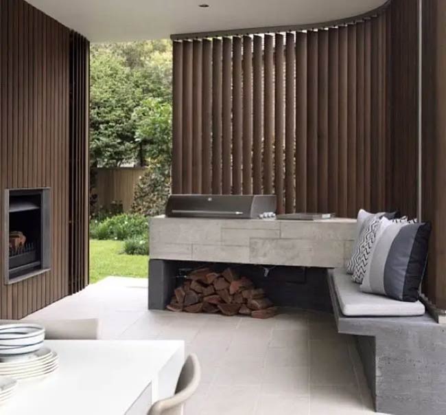 Vertical wood slats curve around the corner to create a stunning backdrop. A floating concrete bench holds the grill and has a spot for firewood underneath. It is a very artistic and modern design.