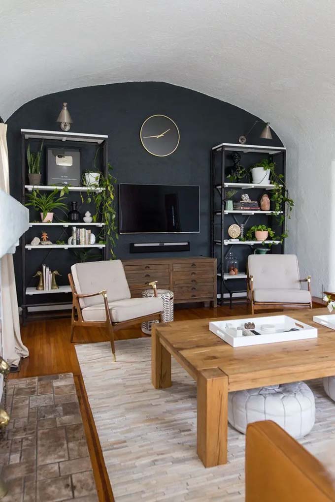 Painting a large black arch on the wall helps the dark TV screen blend in perfectly. Two tall industrial shelves stand on both sides to create a balanced look in this living room. It is a very cool and stylish TV wall decor idea.