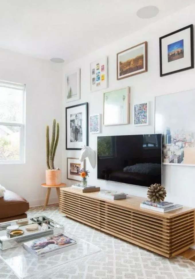 The long wooden console with horizontal slats is a stunning piece of furniture. Colorful art prints and a white deer head fill the wall space with personality. A tall cactus adds a fun desert vibe to this bright and happy TV wall decor.
