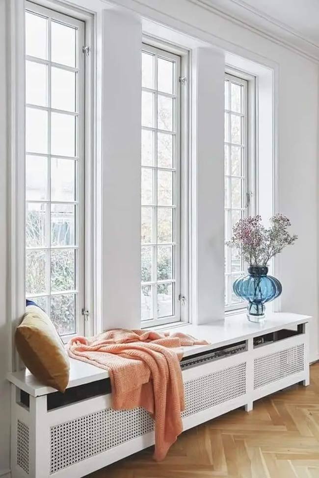 This white cover hides the radiator while providing a wide ledge to sit on. The mesh front allows heat to escape, and the orange blanket adds a nice pop of color.