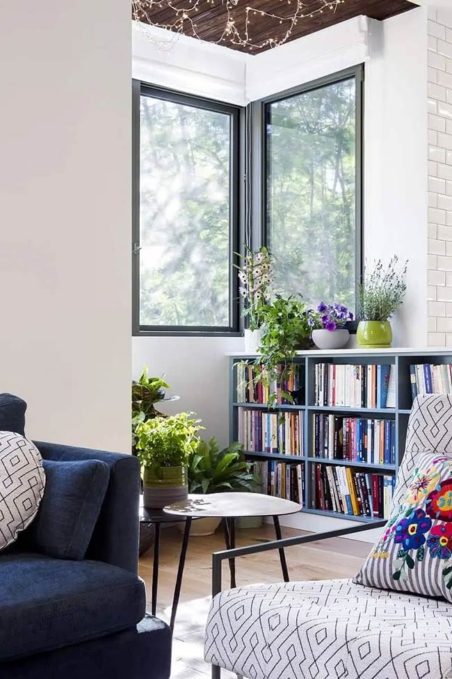 This blue shelving unit fits perfectly into the sunny corner without blocking the view. It holds lots of books and plants to create a peaceful reading area. This is a simple way to add under window storage to an awkward space.